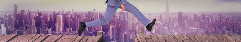 City sky line with a businessman leaping across a gap in the path